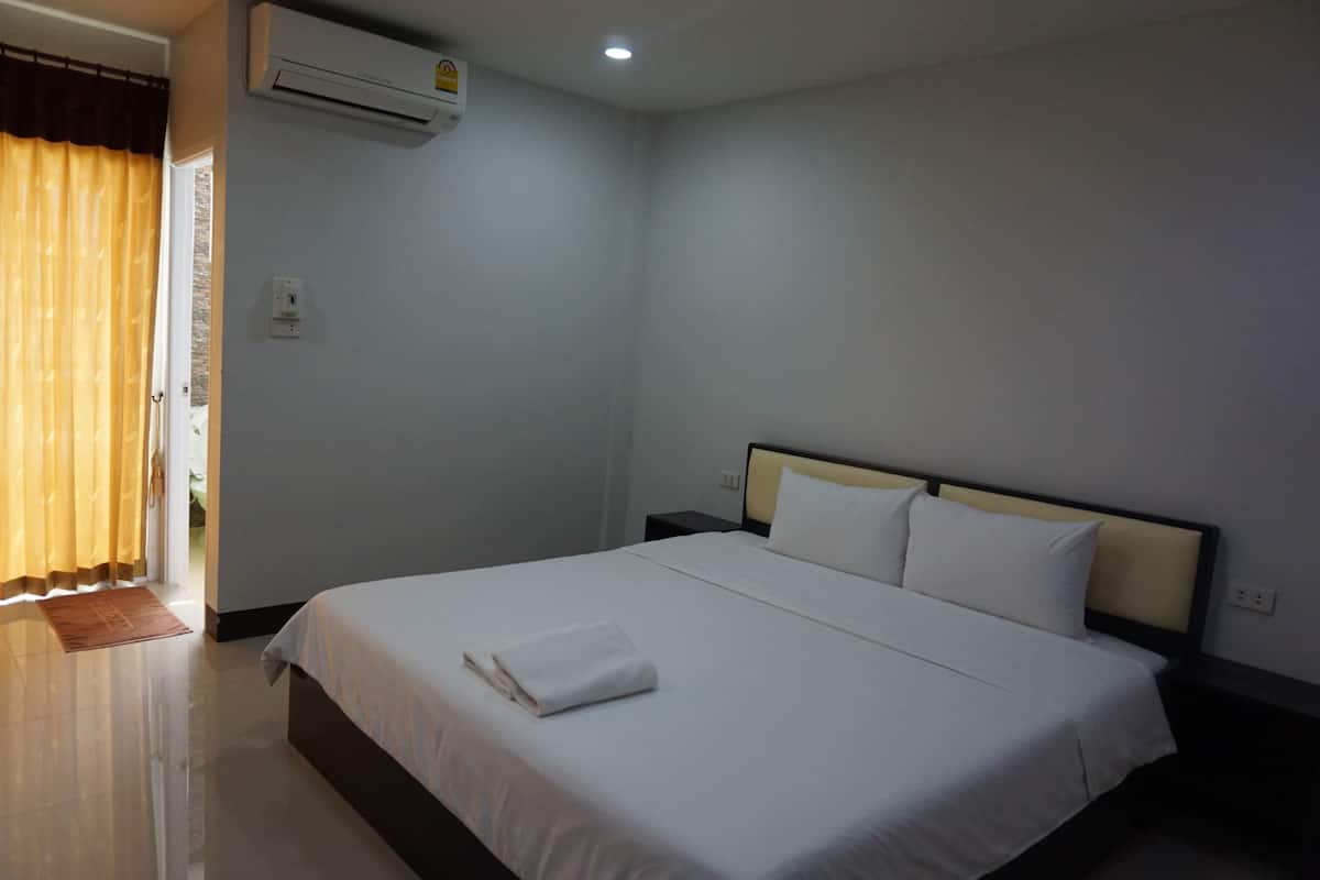 A hotel room with a bed, a nightstand, an air conditioner, and a door with curtains.