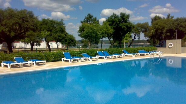 Una piscina con sillas de descanso y un flotador salvavidas en un día soleado.