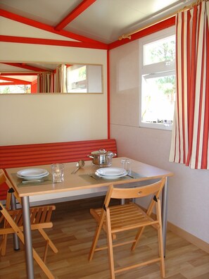 Un área de comedor con una mesa lista para dos personas, sillas de madera, un banco y una ventana con cortinas.