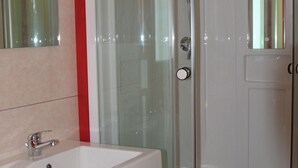 Un baño con ducha envuelta en vidrio, un lavamanos blanco y armarios rojos.