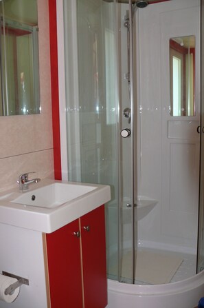 A bathroom with a glass-enclosed shower, a white sink, and red cabinets. - Orbitur Montargil (Ponte de Sor)