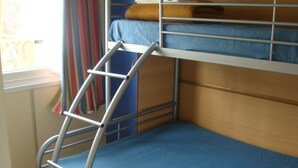 Una cama litera con escalera, ropa de cama azul y una ventana con cortinas.