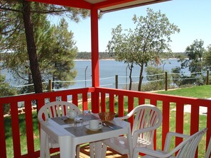 A covered outdoor seating area with a table and chairs, overlooking a body of water. - Orbitur Montargil (Ponte de Sor)