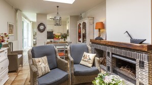 Una sala de estar acogedora con sillones de mimbre, una chimenea y un comedor al fondo.