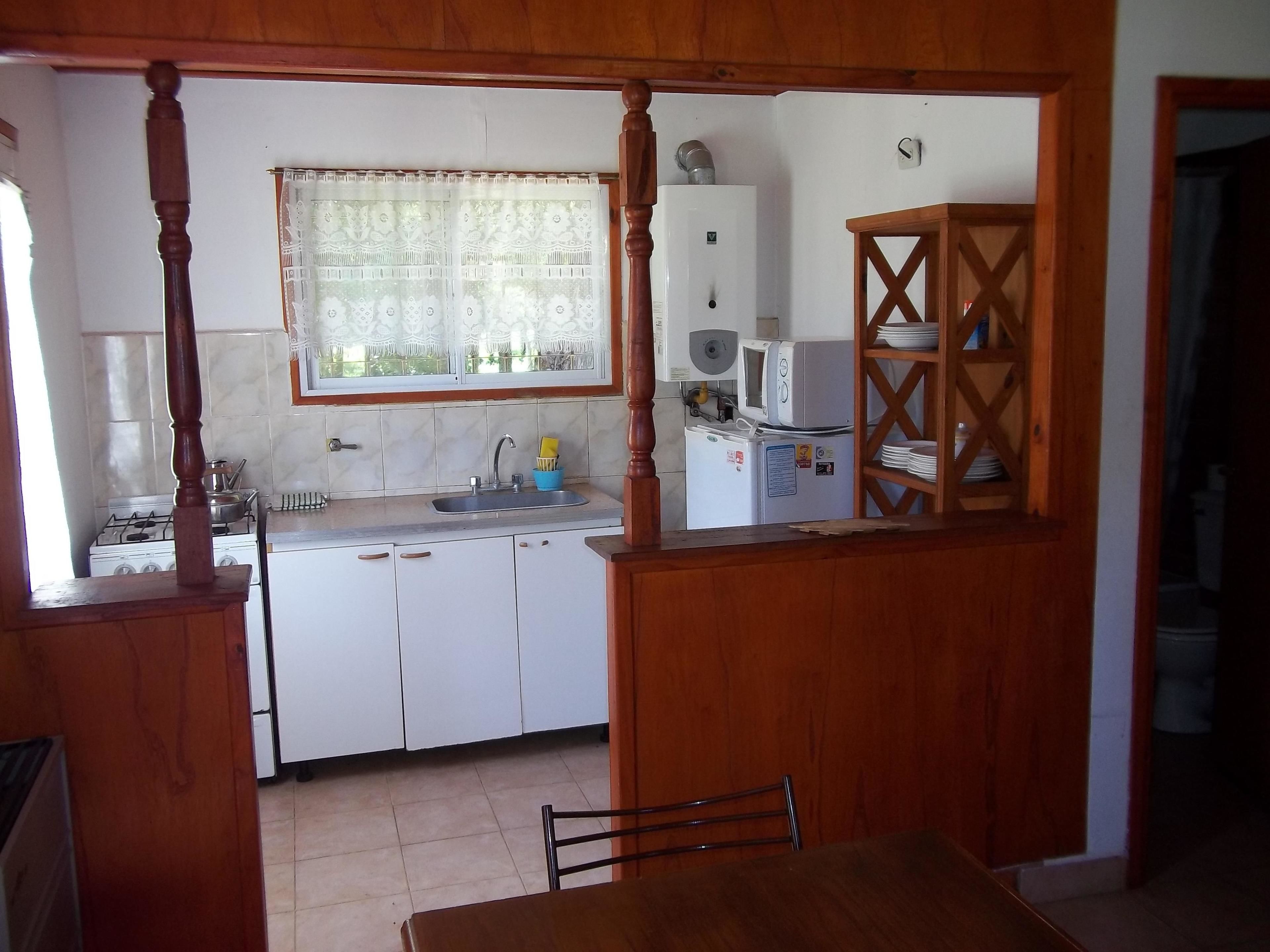 A kitchen with white cabinets, a sink, a stove, and a microwave. There is a window with a curtain, and a wooden cabinet with dishes.