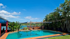 Une piscine dotée d’une terrasse en bois et d’une pergola, entourée d’une végétation luxuriante et offrant une vue sur la mer.