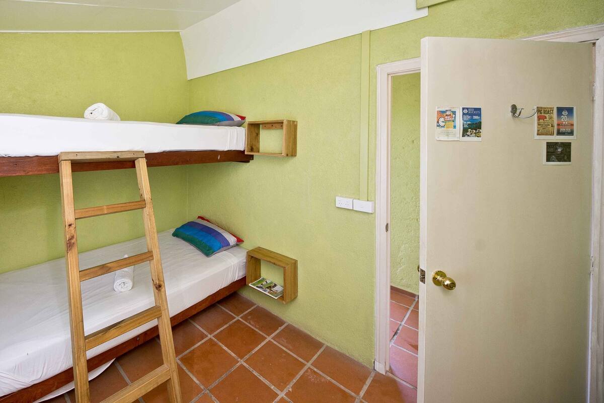 A small, compact room with a bunk bed, a wooden ladder, a small shelf, and a door with a lock.