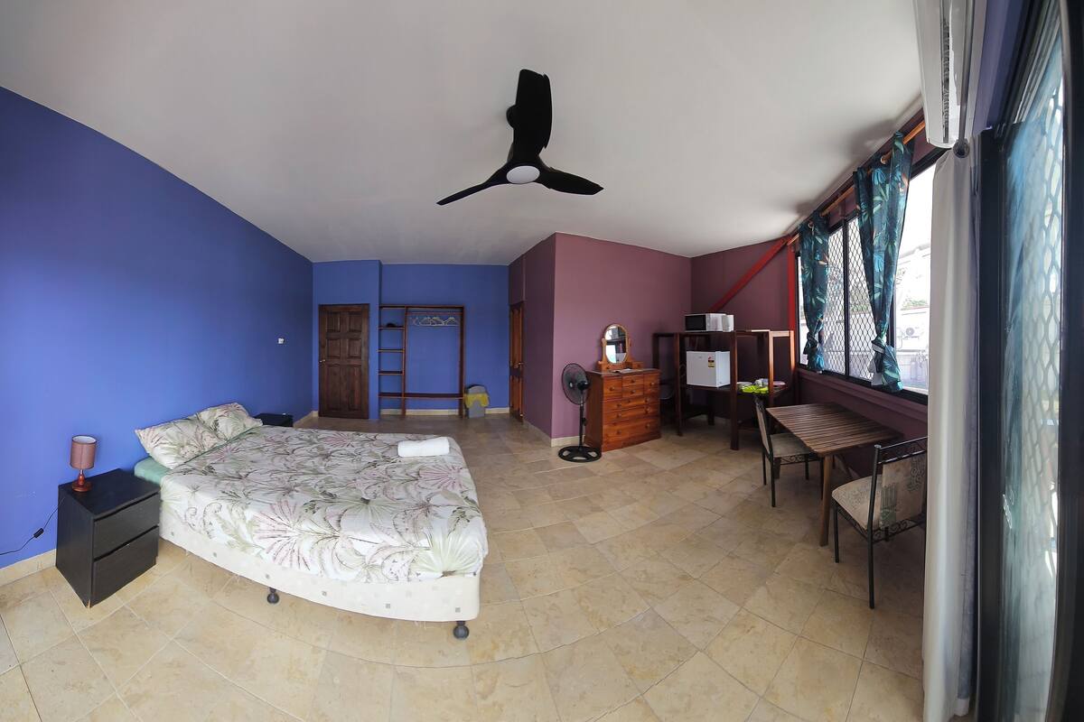 A bedroom with a bed, a desk, a chair, a wardrobe, a ceiling fan, and a window with curtains.