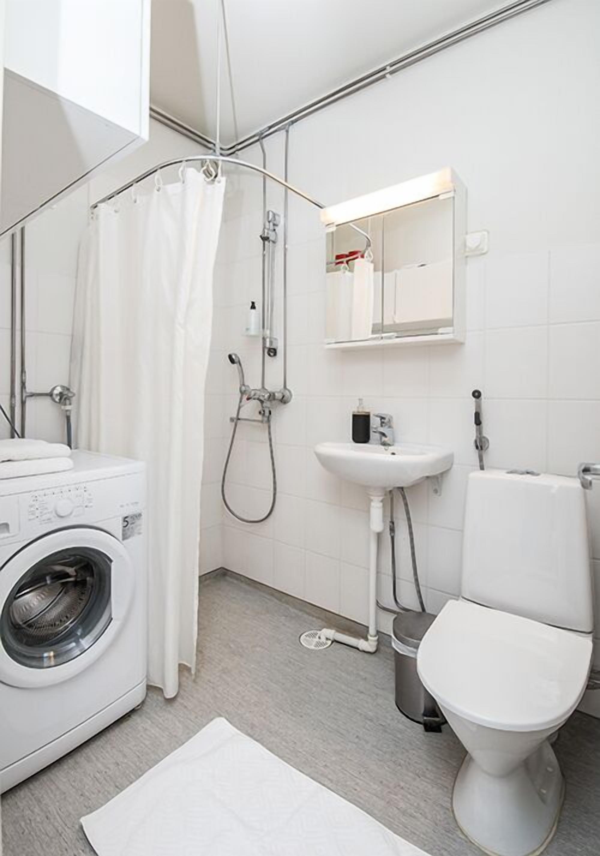 A modern bathroom with a washing machine, a sink, a toilet, and a shower.