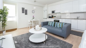 A modern apartment with a grey sofa, white dining table, and a kitchen area.