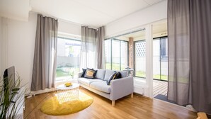 A modern living room with a grey sofa, a yellow rug, and large windows with grey curtains.