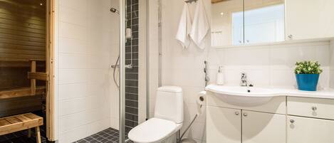 A modern bathroom with a white toilet, a sink, and a mirror. There is a wooden bench and a potted plant on the counter.