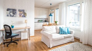 A modern living room with a white sofa, a desk, and a dining area.