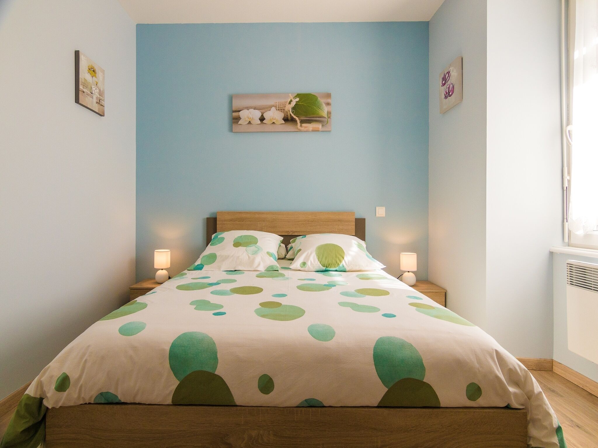 Une chambre à coucher avec un lit, deux tables de chevet, une lampe fixée au mur et une fenêtre.