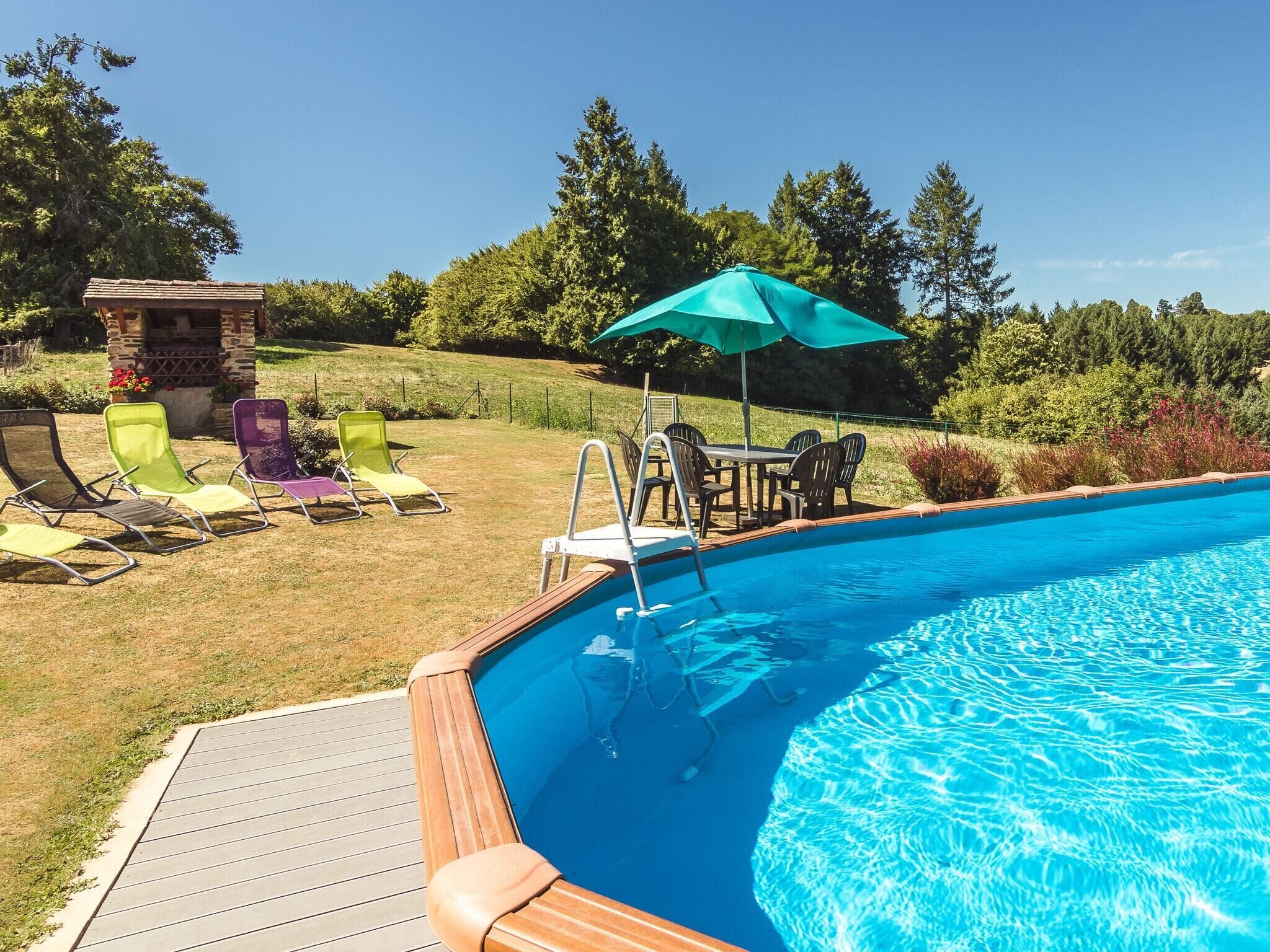 A swimming pool with a wooden deck, surrounded by colorful lounge chairs and a small stone structure.