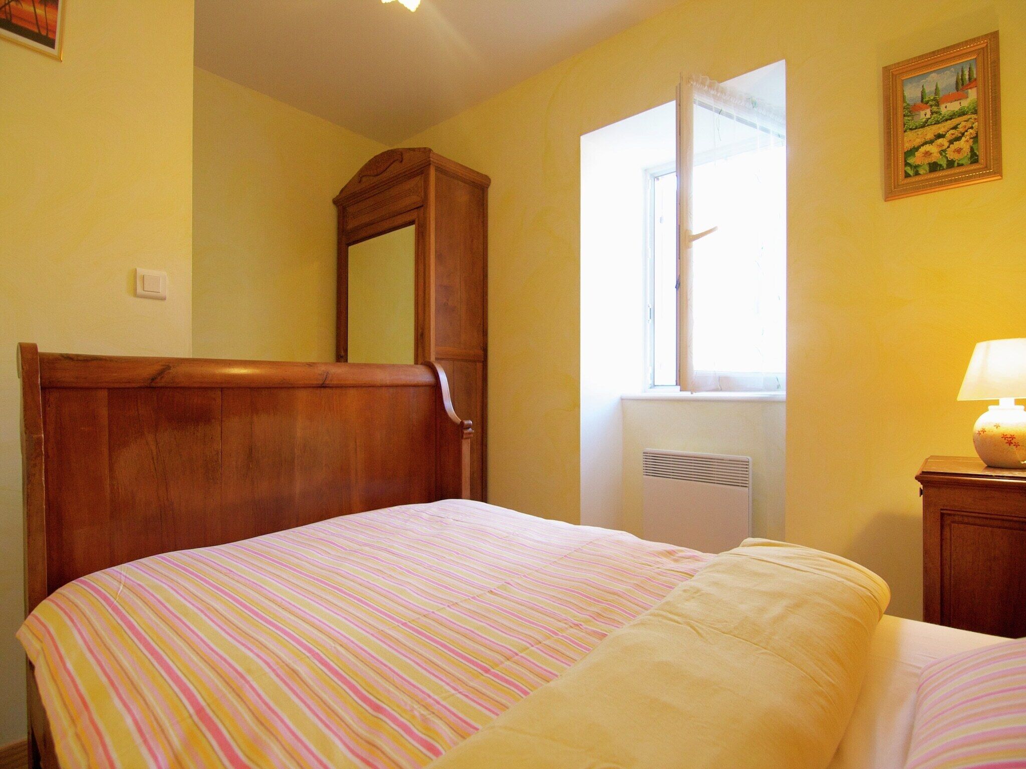 A bedroom with a wooden bed, a window with a view, and a bedside table with a lamp.