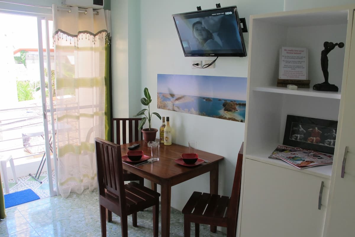 A dining area with a TV mounted on the wall, a potted plant, and a magazine on the shelf.