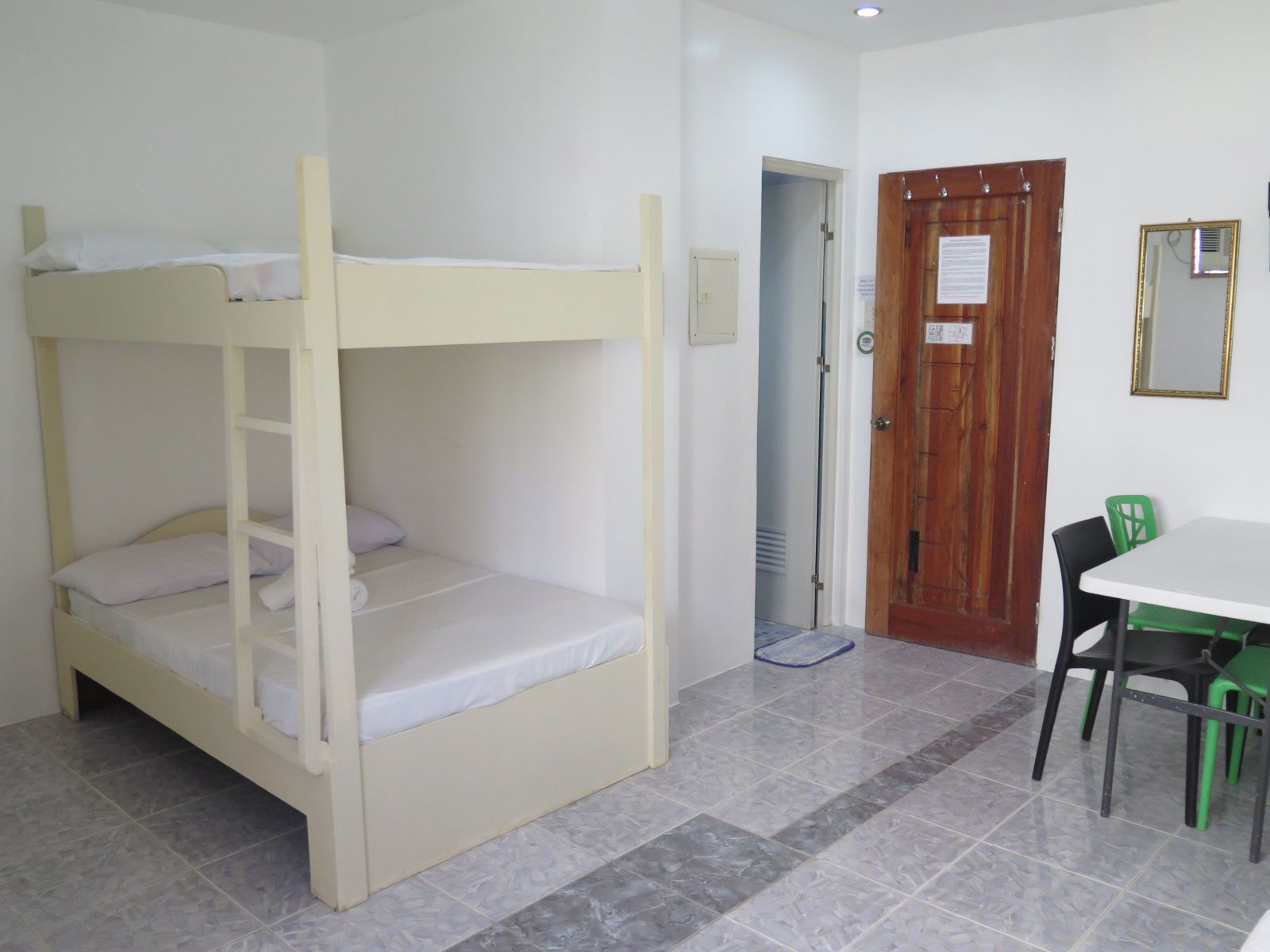 Habitación con literas, una pequeña mesa, sillas, una puerta de madera y un espejo en la pared.