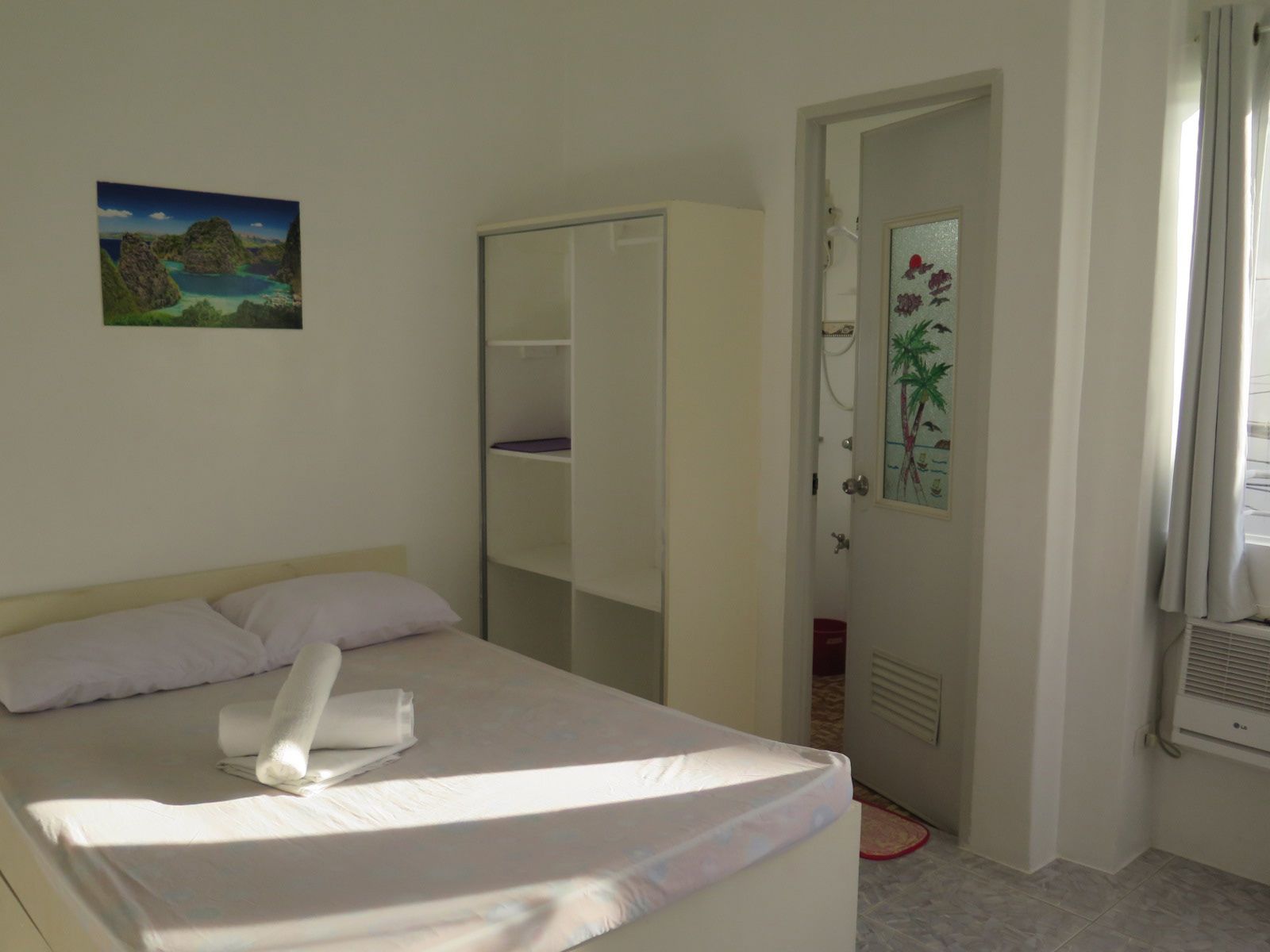 A hotel room with a bed, a wardrobe, a bathroom with a shower, and a painting on the wall.