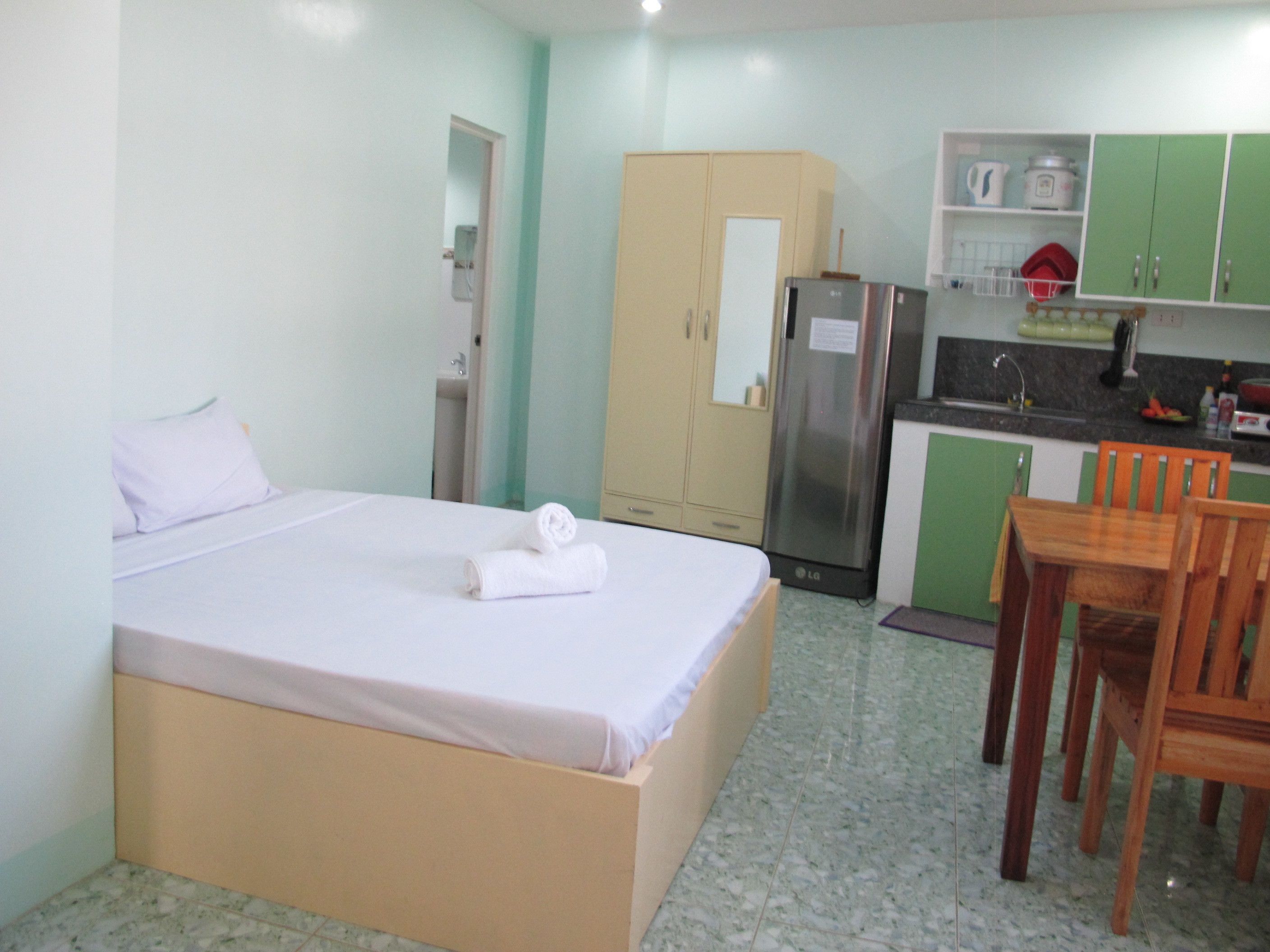 Habitación de hotel con cama, kitchenette pequeño, mesa de comedor con sillas y baño con inodoro y lavabo.