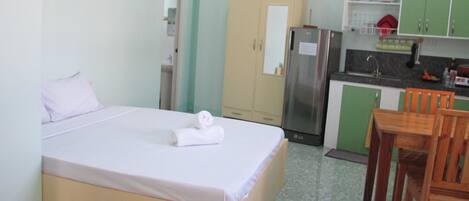 A hotel room with a bed, a small kitchenette, a dining table with chairs, and a bathroom with a toilet and sink.