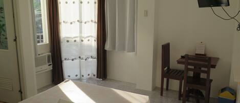 Une chambre d’hôtel comprenant un lit, un bureau avec une chaise, un téléviseur fixé au mur et une fenêtre avec des rideaux.