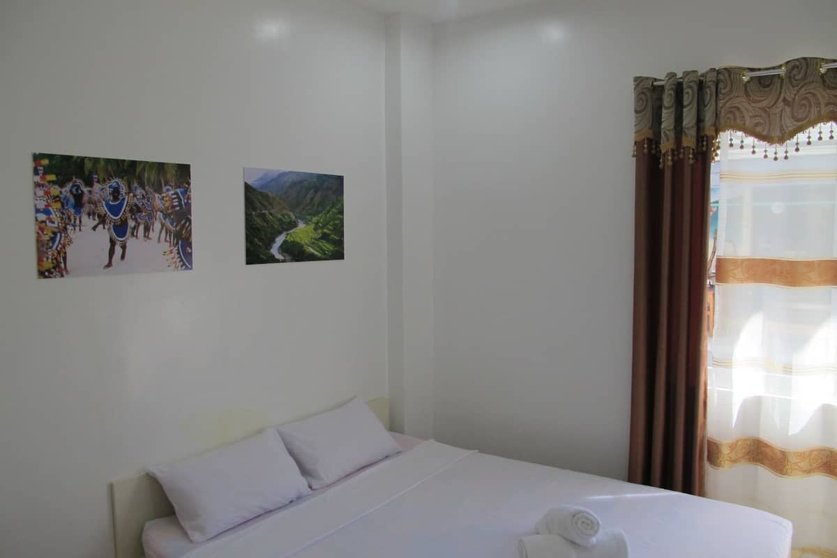 A bedroom with a bed, pillows, and a neatly folded towel. There are two framed pictures on the wall.
