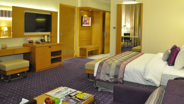 A hotel room with a bed, a desk, a chair, a television, and a small table with magazines. - Fortune Park Hotel (Dubai)