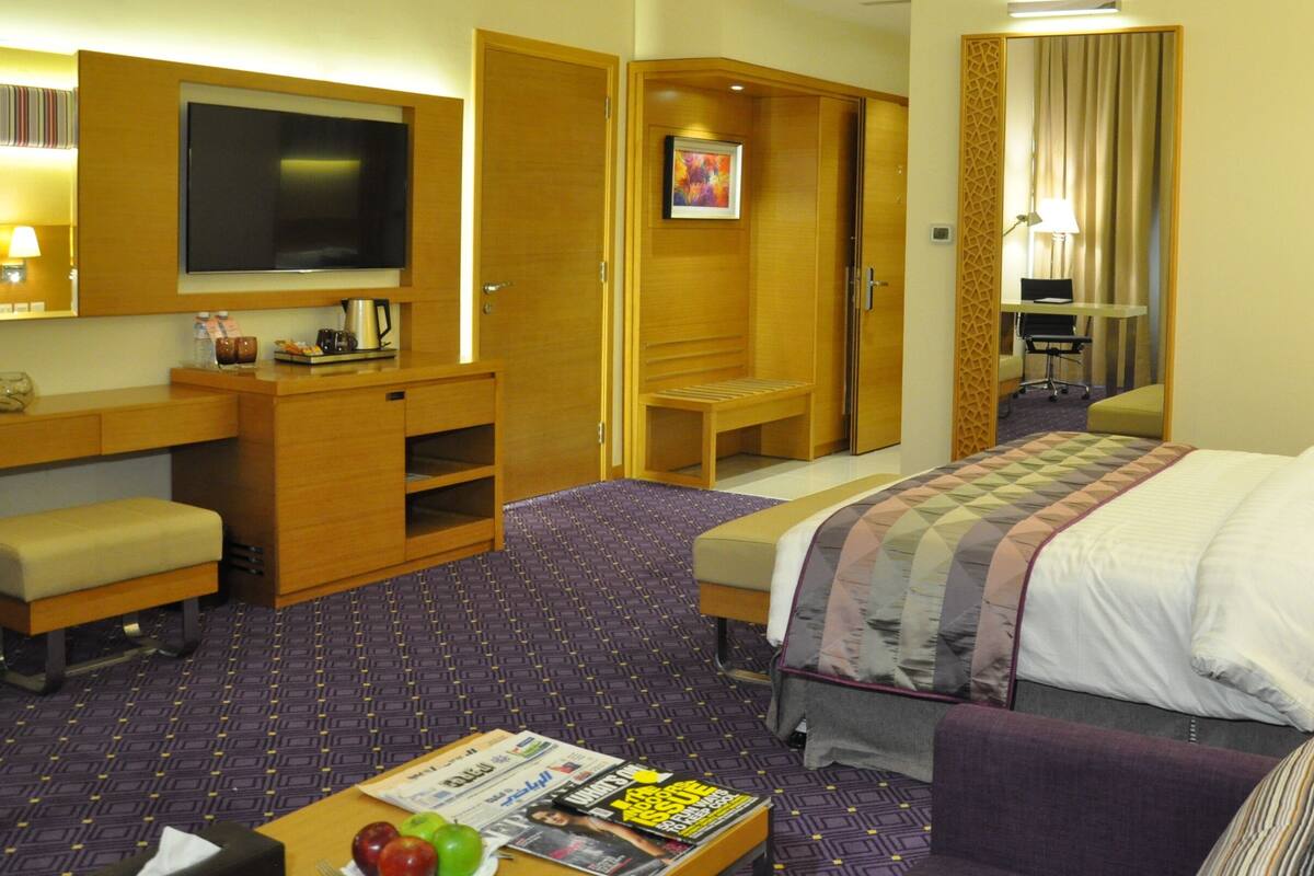 Hotelkamer met een bed, bureau, stoel, televisie en een klein tafeltje met tijdschriften.