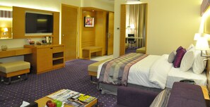 A hotel room with a bed, a desk, a chair, a television, and a small table with magazines. - Fortune Park Hotel (Dubai)