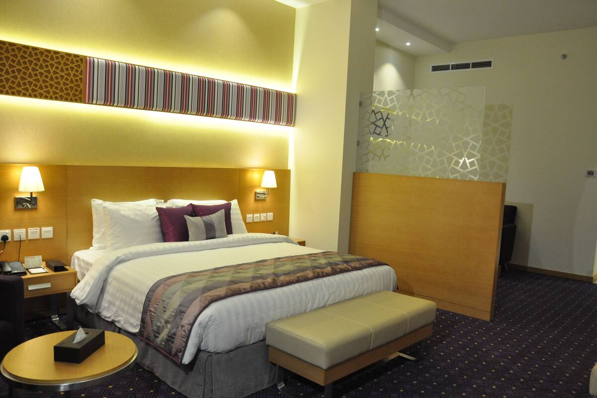Een hotelkamer met een groot bed, bedlampjes, een bureau en een klein rond tafeltje.