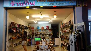 Uma loja com prateleiras cheias de bolsas e sapatos, uma televisão no centro, e uma mulher olhando.