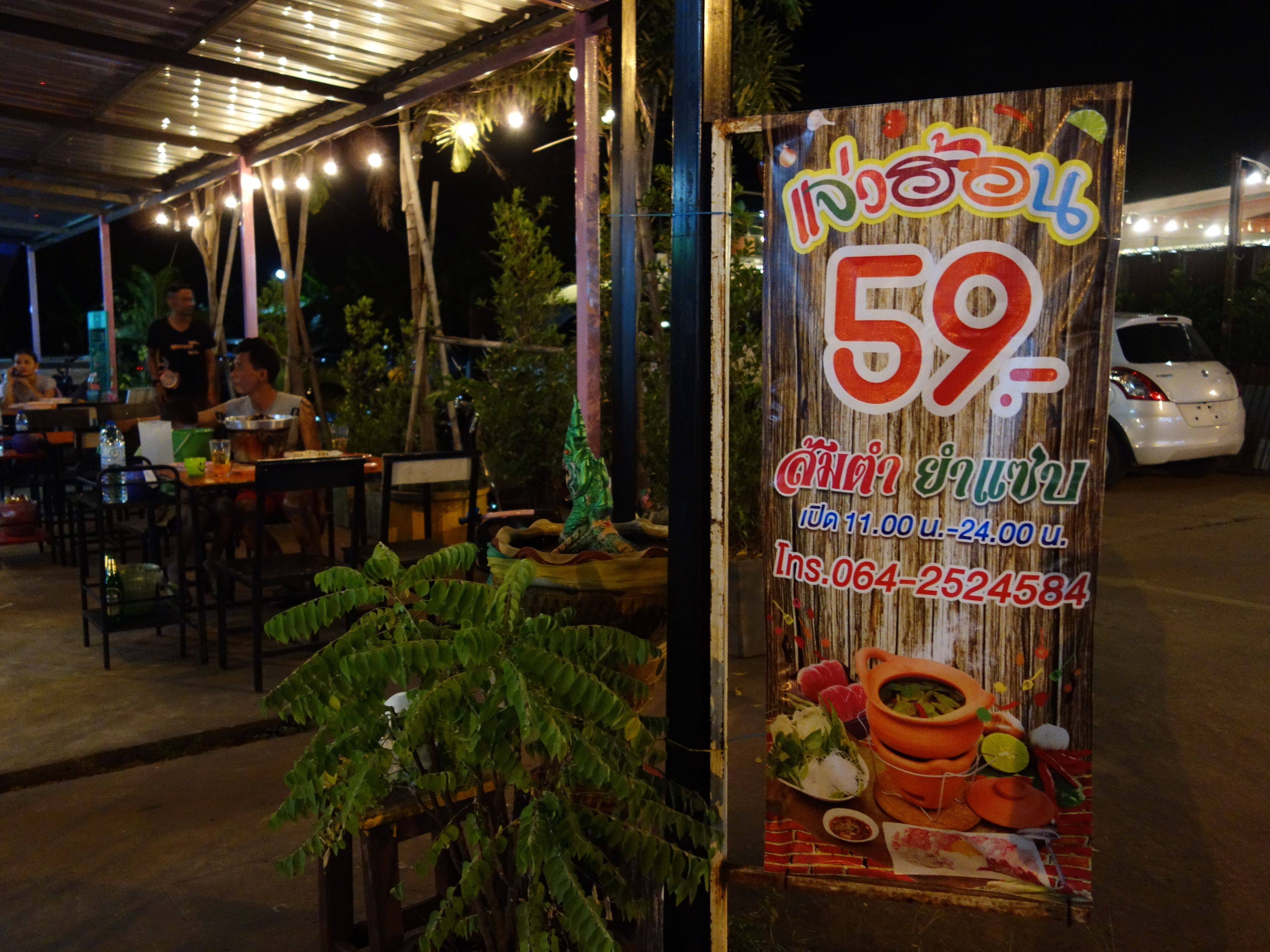 An outdoor restaurant with a wooden signboard displaying a price and operating hours.