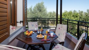 A wooden balcony with a table set for breakfast, including fruits, pastries, and drinks.