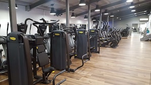 Un gimnasio con varias máquinas de ejercicio, suelo de madera e iluminación en el techo.