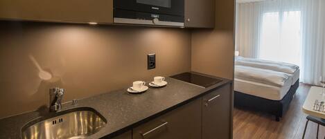 Una habitación de hotel moderna con kitchenette, una cama y zona de comedor.
