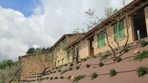 A hillside building with multiple windows and green shutters, surrounded by a landscaped area with small shrubs and trees. - Pekko Country House (Spello)