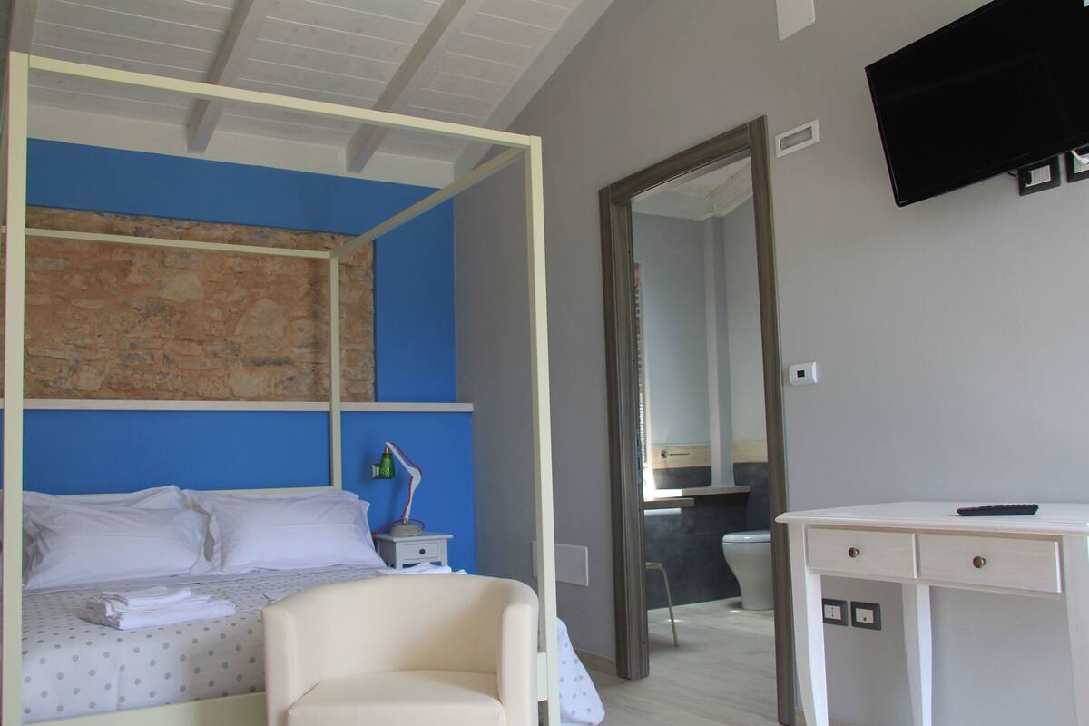 A bedroom with a bed, a desk, a mirror, and a TV.