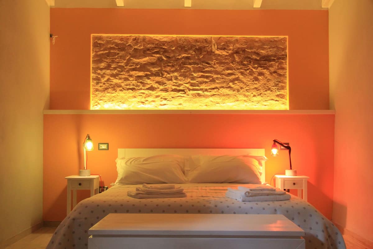 A bedroom with a bed, two bedside tables, a nightstand, a wall-mounted light, and a wall art piece.
