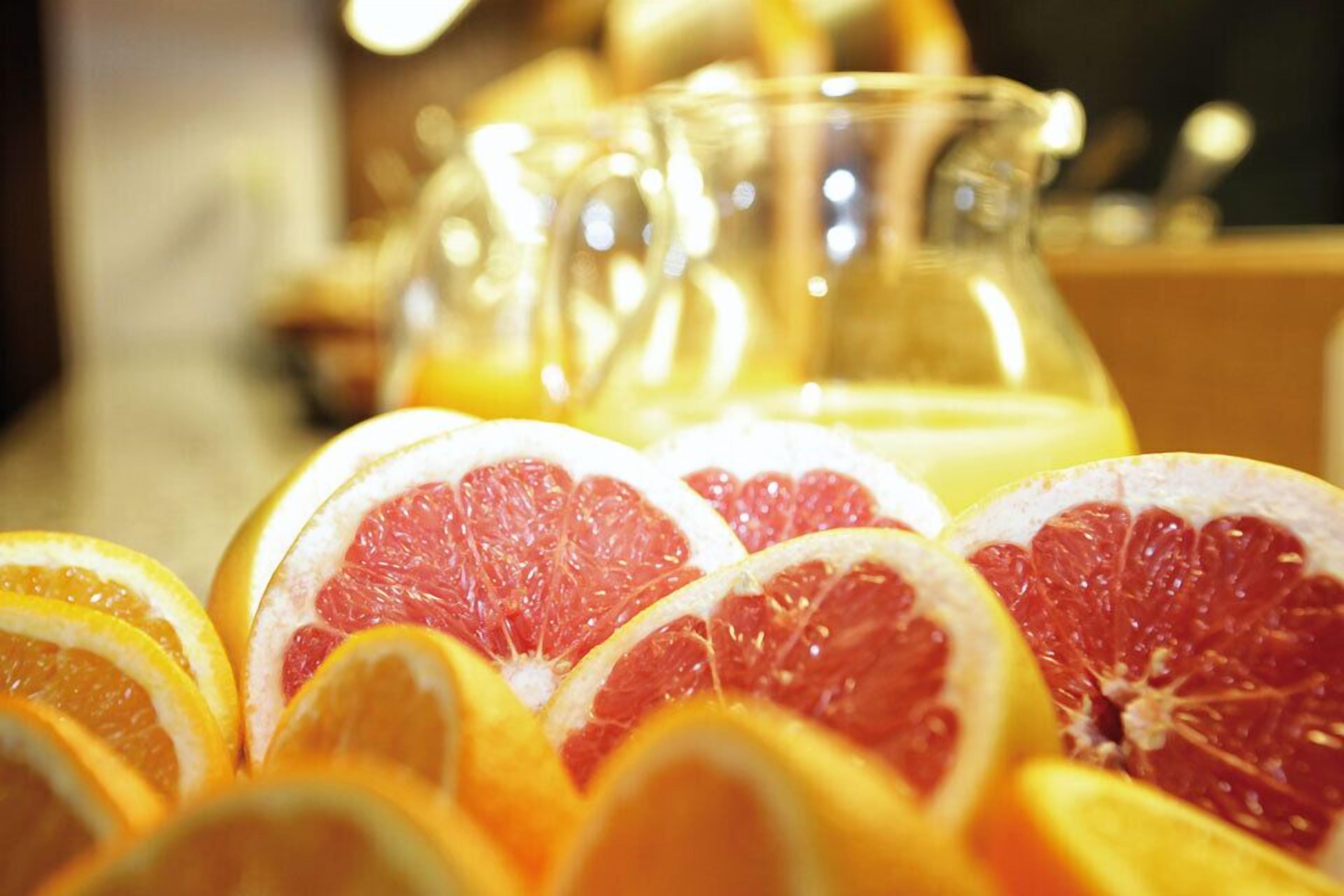 A close-up of sliced oranges and grapefruits with a glass pitcher in the background.