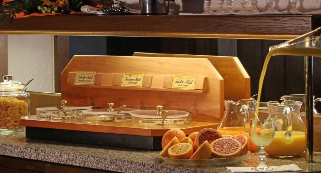 A breakfast buffet with labeled containers for different types of milk, a pitcher of orange juice, and fresh fruits like oranges and grapefruit.