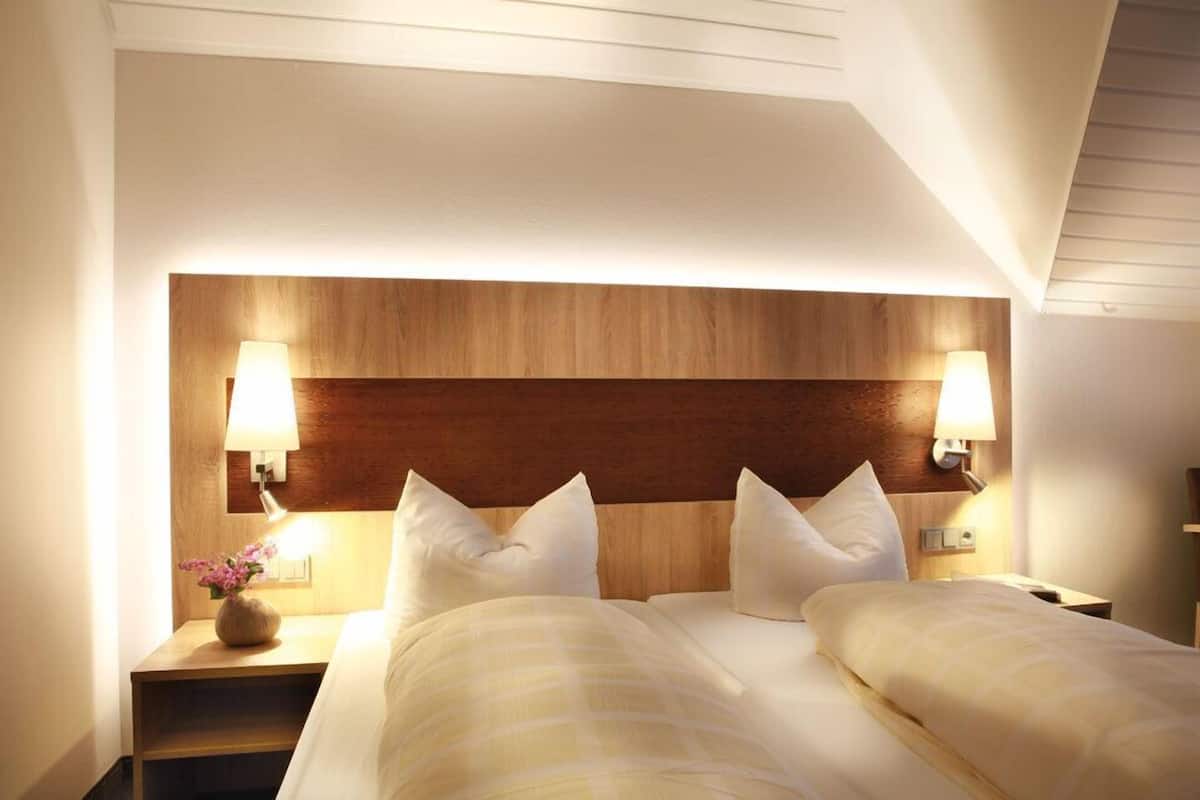 Ein Hotelzimmer mit einem hölzernen Kopfteil, zwei Betten mit weißer Bettwäsche, Nachttischlampen und einem Nachttisch mit einer Blumenvase.