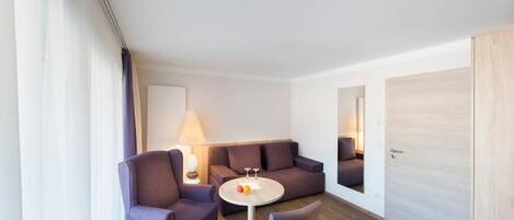 Una habitación de hotel moderna con un sofá, dos sillones, una mesita redonda y una lámpara.