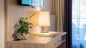 Een hotelkamer met een houten bureau, een televisie waarop 'WELKOM' staat, een lamp en een plant.