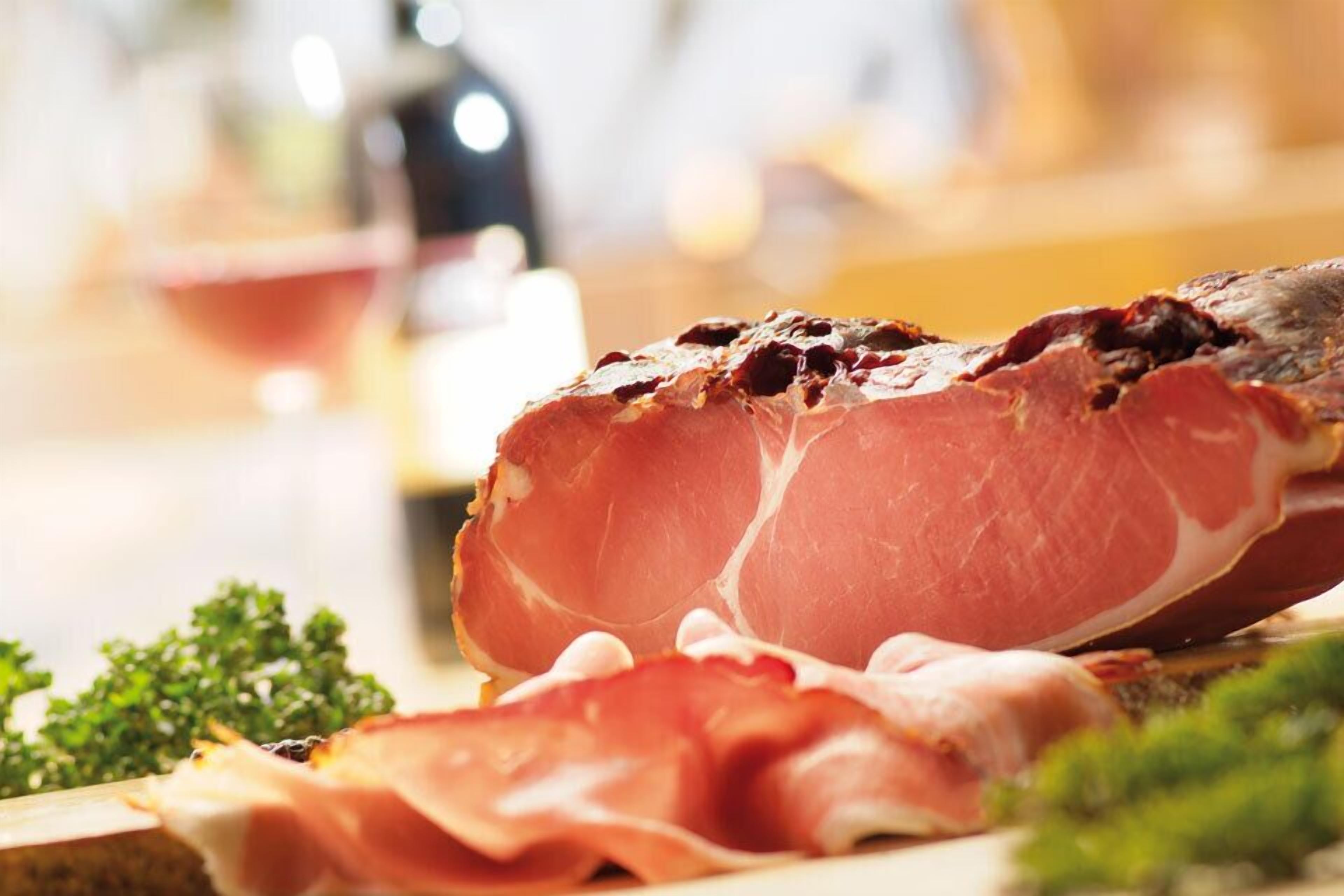 Primer pla de talls de pernil salat, probablement prosciutto, amb un fons borrat que suggereix un ambient de menjador.