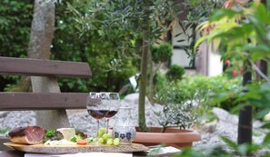 Un montaje para picnic con un banco de madera, un plato de queso, uvas y una botella de vino, rodeado de follaje.