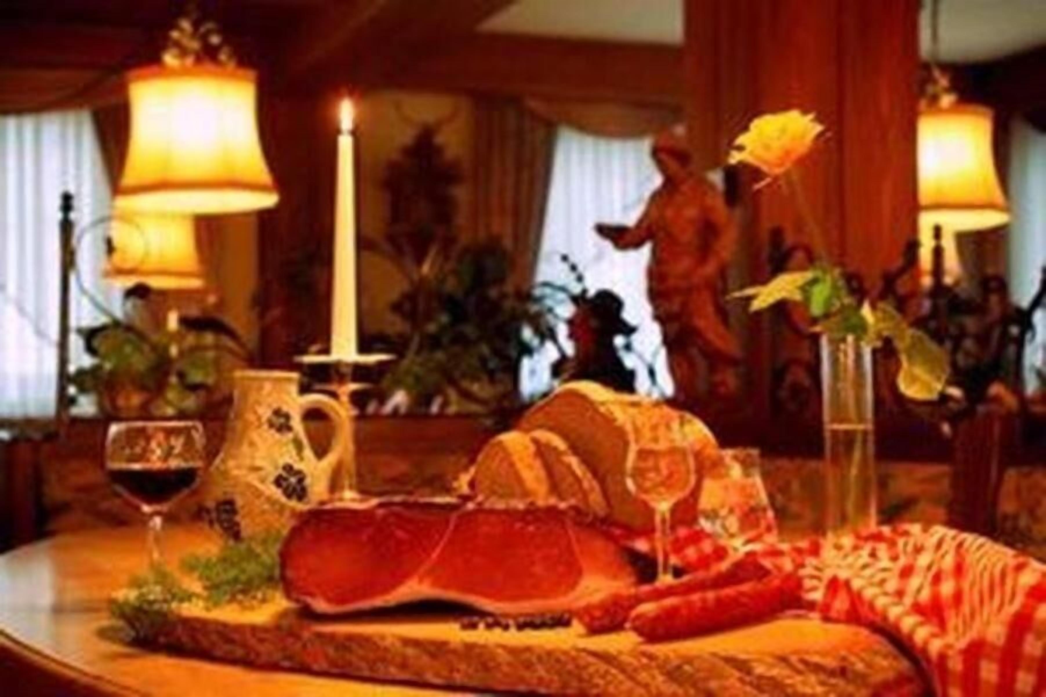 A dining table with a variety of food items, including a large piece of meat, a pitcher, and a glass of red wine.