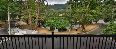 A view from a balcony overlooking a road with a river, trees, and a hilly landscape in the background.