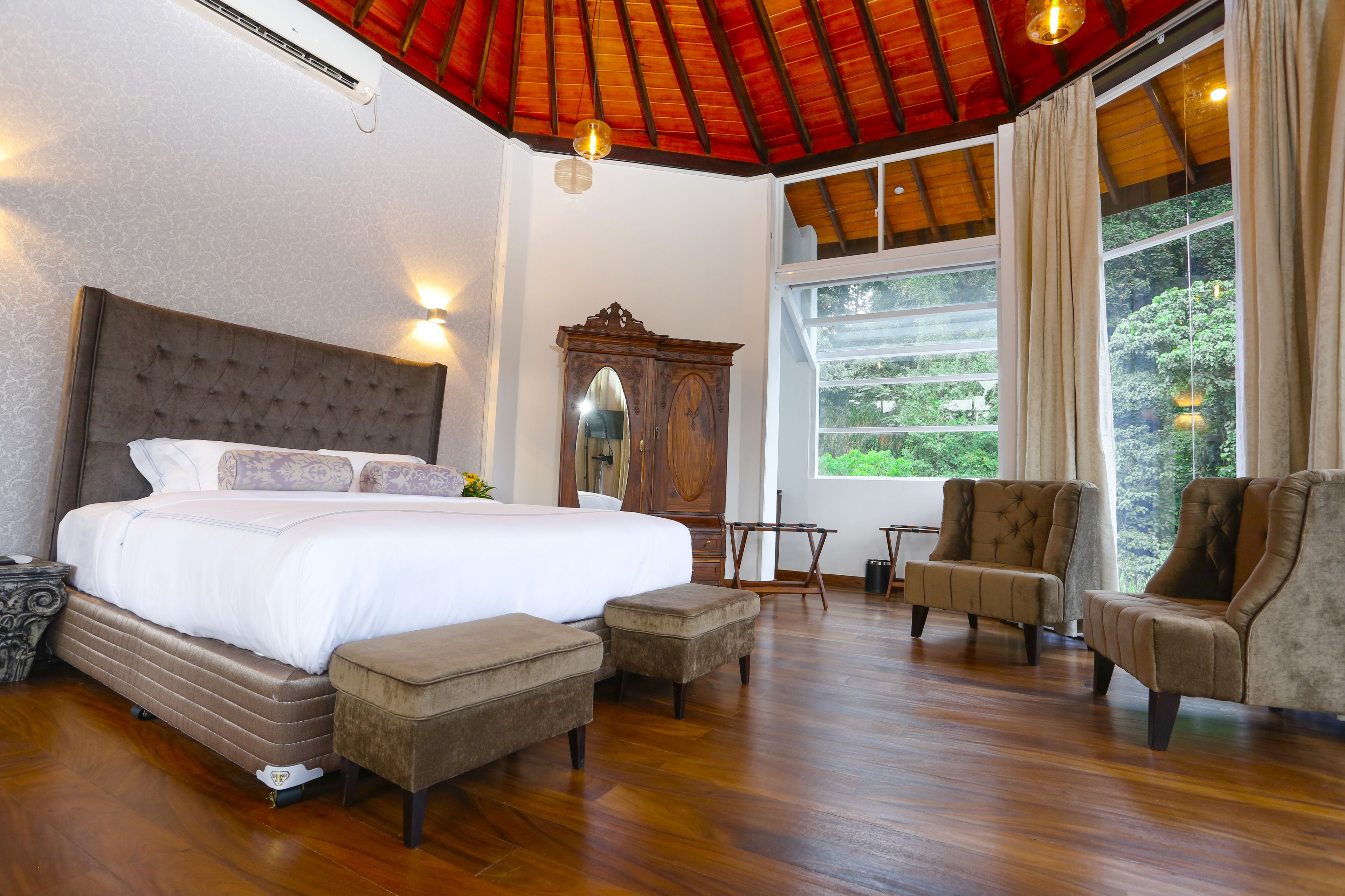 A spacious bedroom with a large bed, a wooden wardrobe, and a seating area with chairs and a table.