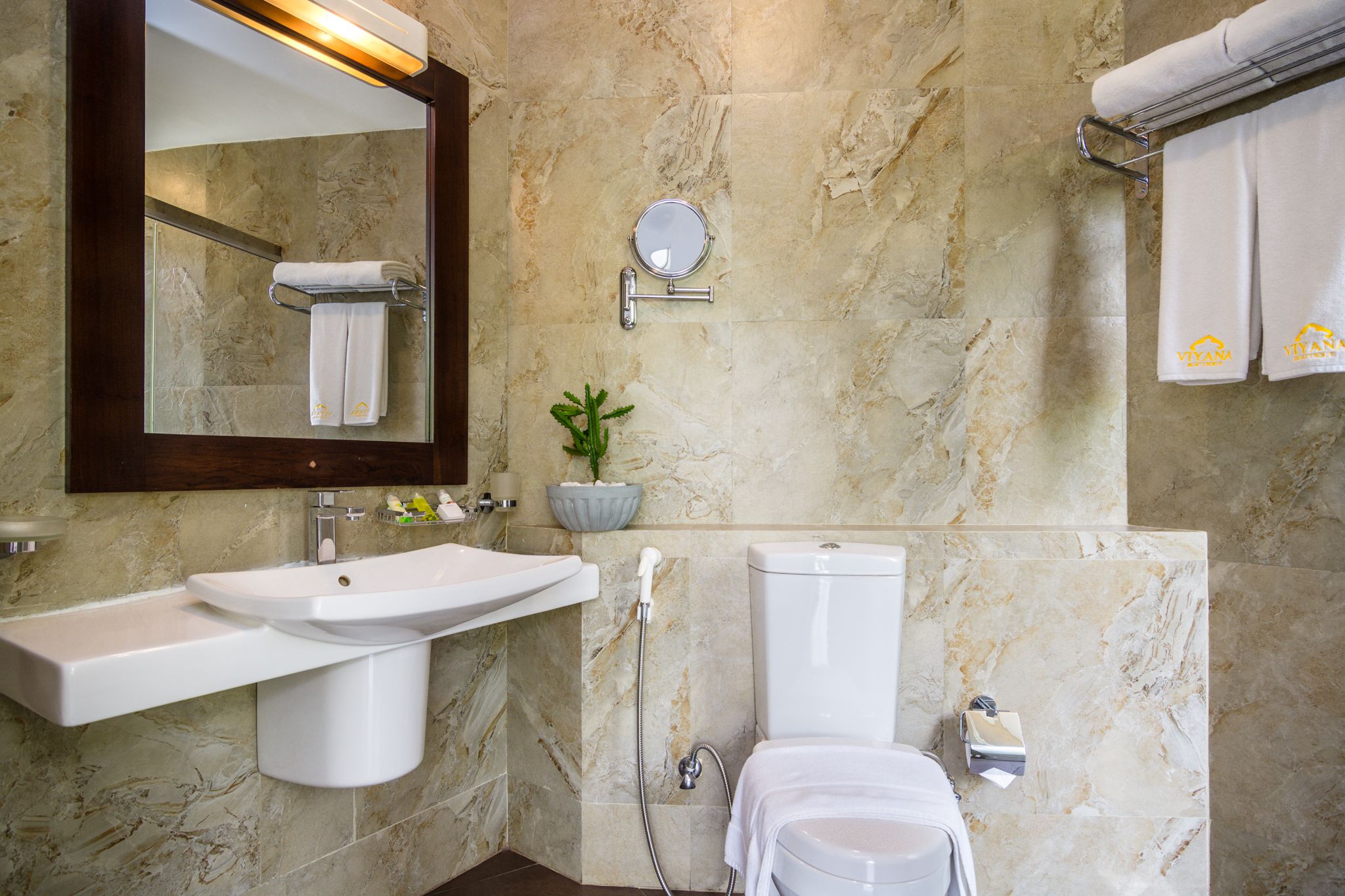 A bathroom with a marble wall, a sink, a toilet, a towel rack, and a mirror.